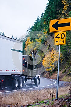 Black big rig semi truck on autumn road in raining weather