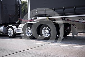 Black big rig semi truck with chrome wheels and fenders and black tented frame semi trailer going by roadway