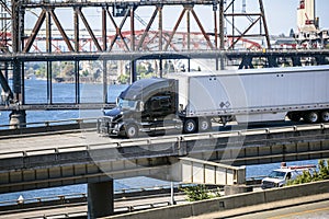 Black big rig semi truck with dry van semi trailer transporting cargo running on the overpass road along the Willamette River in