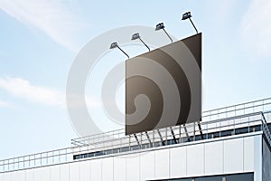 Black billboard with copyspace with backlights on industrial building rooftop outdoor at blue sky background. 3D rendering, mockup