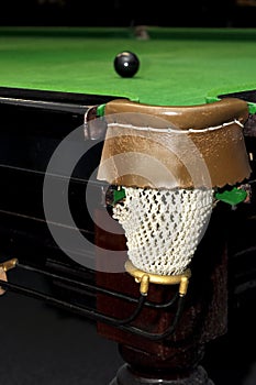 Black billiard ball in front of corner pocket on green baize table