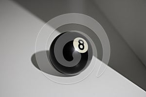 Black billiard ball on white surface with hard ligt