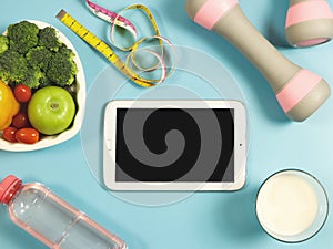 Black blank screen computer tablet , vegetables and fruit in heart shape plate, bottle of water, measure tape,  pink dumbbells and