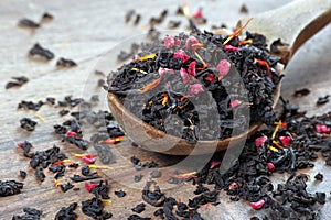Black blended tea with flower petals and dried fruit on a wooden spoon.