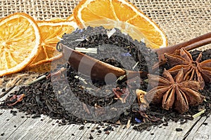 Black blended tea with flower petals and dried fruit in wooden spoon on wooden desk. Black tea, anise stars and dried oranges