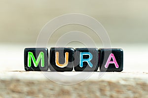 Black block with word mura on wood background