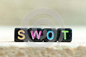 Black block with word swot abbreviation of strength, weakness, opportunities, threats on wood background