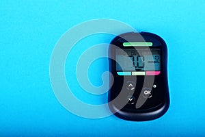 Black blood glucose meter shows high blood sugar content, lying on a blue background