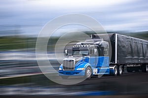 Black and blue stylish big rig semi truck transporting commercial cargo in covered black semi trailer