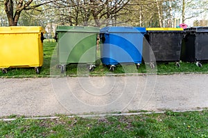 Black, blue, yellow, green garbage recycling bins on street in city. Segregate waste, sorting garbage.