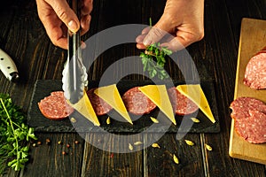 Black board serving concept with cheese, sausage and parsley appetizer. Cooking a delicious dinner with the hands of a chef on the