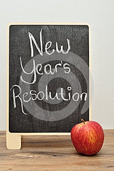A black board with the words new years resolution and an apple