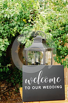 Black board wtih white welcome sign on wooden table with vintage alntern and green background