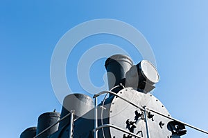 Black boiler of a steam locomotive against the background of clear blue sky. You can see an electrical headlight, chimney or