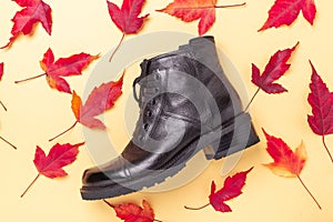 Black boot and red leaves on a yellow background. Autumn sale concept
