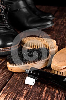 Black boots on wooden background with polishing equipment, brush and polish cream.