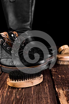 Black boots on wooden background with polishing equipment, brush and polish cream.