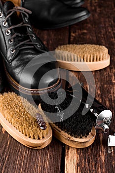 Black boots on wooden background with polishing equipment, brush and polish cream.