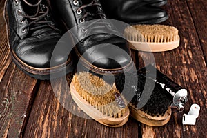 Black boots on wooden background with polishing equipment, brush and polish cream.