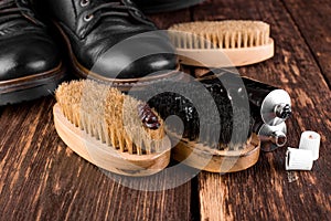 Black boots on wooden background with polishing equipment, brush and polish cream.