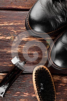 Black boots on wooden background with polishing equipment, brush and polish cream. Top view. Flat lay