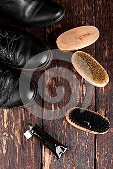 Black boots on wooden background with polishing equipment, brush and polish cream. Top view. Flat lay