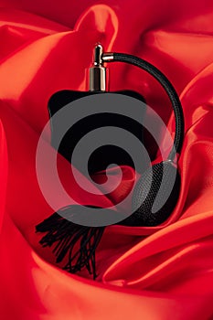 Black bottle eau de toilette or perfume with long tassel spray pomp lies on red background of flowing fabric, vertical