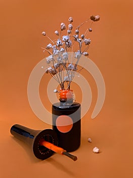 Black bottle of nail polish on a orange background with flowers