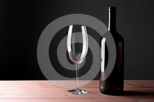 Black bottle of red wine and a glass. A bottle of wine stands on a table, a bottle on a gray background and a wooden table