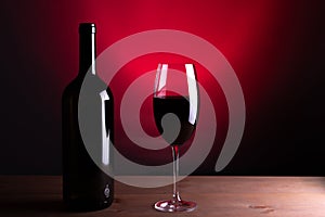 Black bottle of red wine and a glass. A bottle of wine stands on a table, a bottle on a gray background and a wooden table. Red