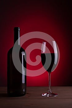 Black bottle of red wine and a glass. A bottle of wine stands on a table, a bottle on a gray background and a wooden table. Red