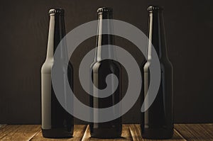 black bottles of beer on a wooden table against a dark background/black bottles of beer on a wooden table against a dark