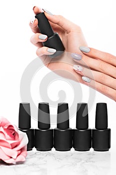 Black bottles of nail polish on a background of flowers. Manicure design.