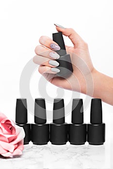 Black bottles of nail polish on a background of flowers. Manicure design.