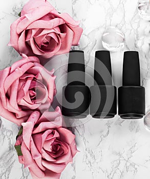 Black bottles of nail polish on a background of flowers. Manicure design.