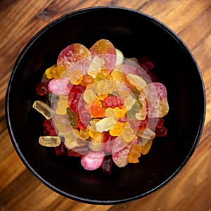 Black bowl with colorful sweet candy like gummibears on a wooden plate