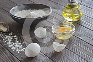 Black bowl with flour. Glass bottle with butter, eggs, wooden spoon with flour