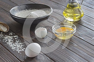 Black bowl with flour. Glass bottle with butter, eggs, wooden spoon with flour