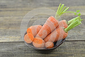 Black bowl with fresh carrots and cut on wooden table, closeup