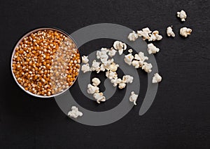 Black bowl with raw sweet corn and popcorn on wood