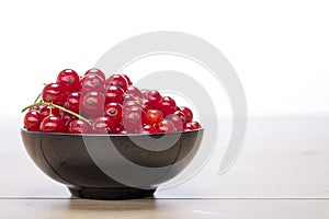 Black bowl with redcurrants on a wood table