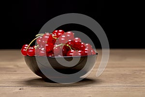 Black bowl with redcurrants on a wood table