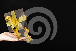 A black box with a golden ribbon on a dark background levitates over a woman`s hand. Gift box for gifts on black Friday. Flying