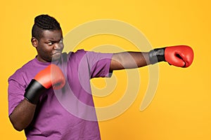 Black boxer guy throwing punch wearing boxing gloves, yellow background