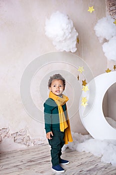 Black boy in a green sweater and a yellow scarf smiling. Portrait of a little African American. Baby smiles. A black boy stands ne