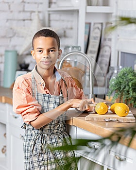 Black boy kid cooking fresh lemon on kitchen at home. African child preparing on table.