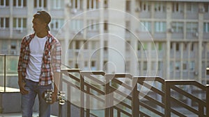 Black boy with skate walking alone on street, missing friends, feeling lonely