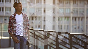 Black boy with skate walking alone on street, missing friends, feeling lonely