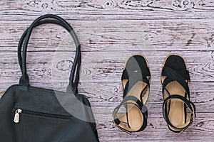 Black braided women`s shoes and bag on wooden background.