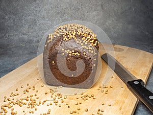 Black bread sprinkled with coriander. Borodino bread whith knife. Flour product. Bread with spices on kitchen board on black